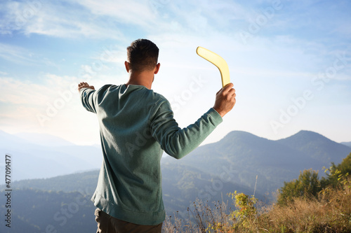 Man throwing boomerang in mountains on sunny day, back view photo
