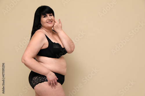 Beautiful overweight woman in black underwear on beige background, space for text. Plus-size model