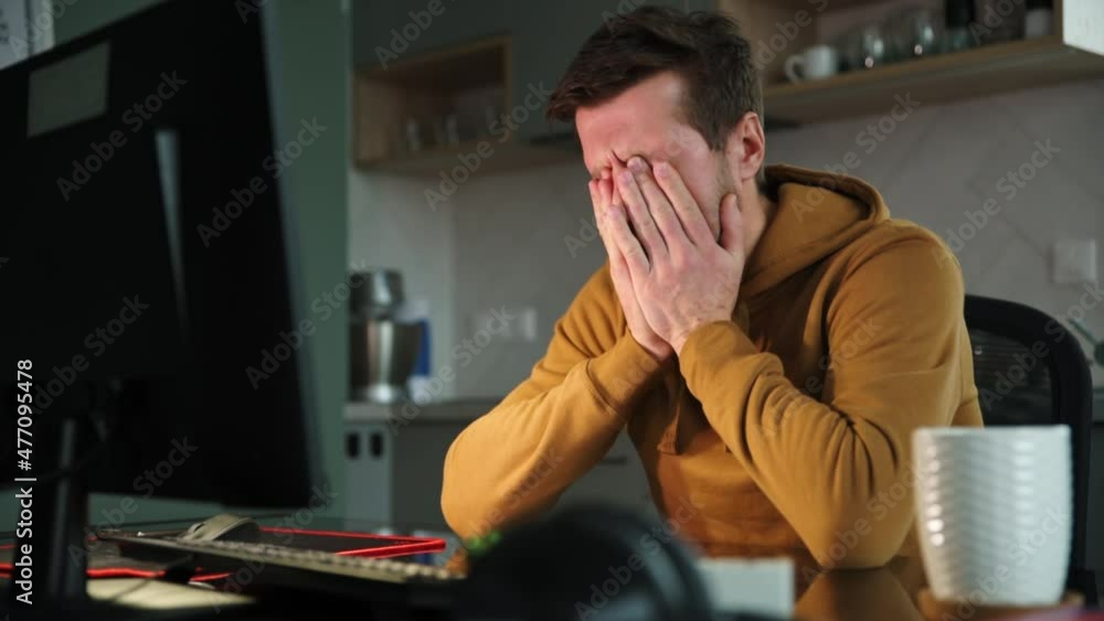 Man sitting at table at home office and works with computer. Freelancer remotely working late. Emotional stress and burnout Man sitting at table at home office and works with computer. Freelancer remotely working late. Emotional stress and burnout