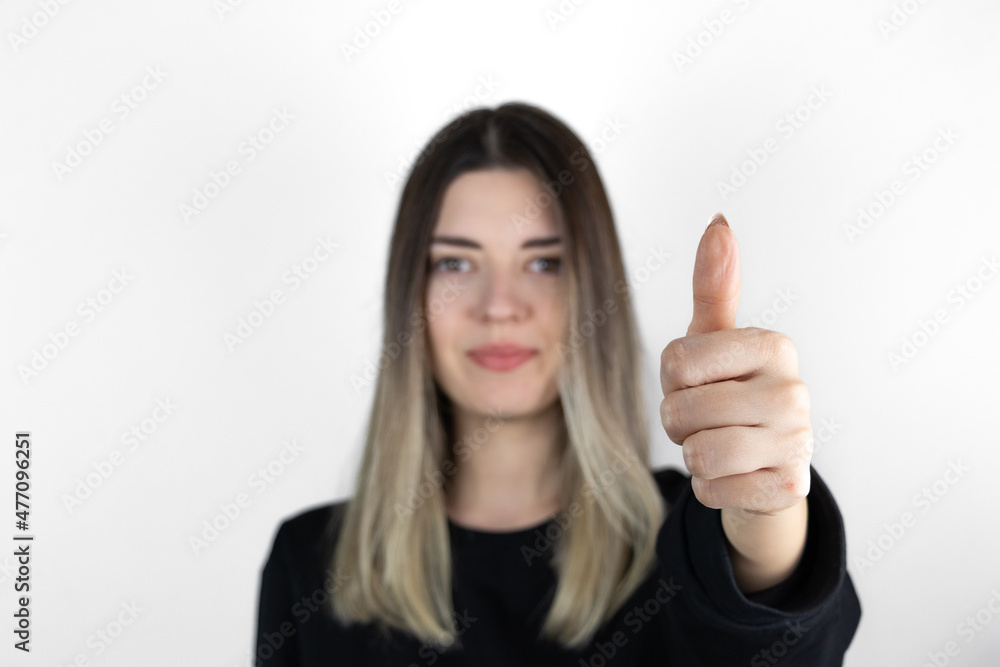 Young girl giving thumbs up. Girl with no emotions posing with thumbs up looking at camera. White studio background. The focus is on her hand. Young girl giving thumbs up. Girl with no emotions posing with thumbs up looking at camera. White studio background. The focus is on her hand.