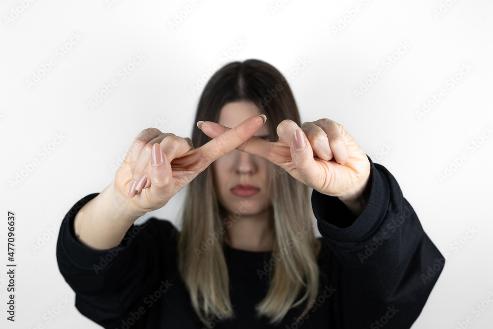 Blonde girl is making a forbidden sign with fingers. 