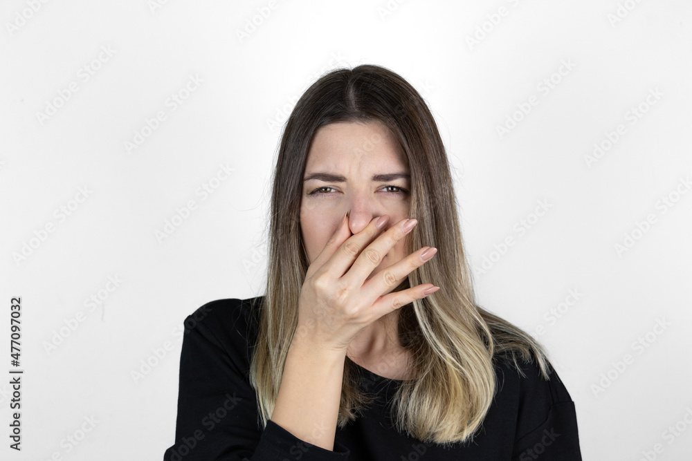 Displeased woman covers nose with hand, smells something awful, pinches nose, frowns in displeasure, sees pile of garbage, dressed in casual clothes, isolated on white background. Bad odour. Displeased woman covers nose with hand, smells something awful, pinches nose, frowns in displeasure, sees pile of garbage, dressed in casual clothes, isolated on white background. Bad odour.