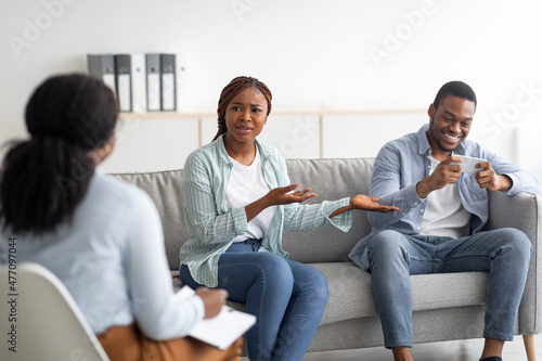 Irritated black woman complaining about her husband's smartphone addiction during psychological consultation © Prostock-studio