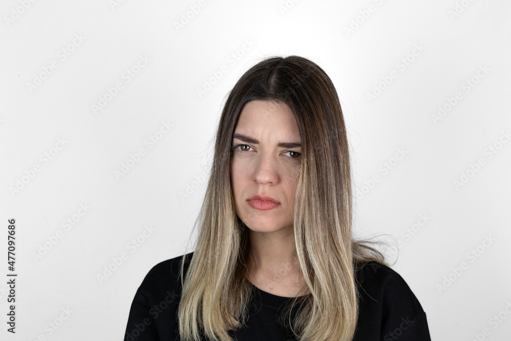Young girl with serious and angry expression on her face. She is in anger. She asked something and she is waiting answer. White studio background.