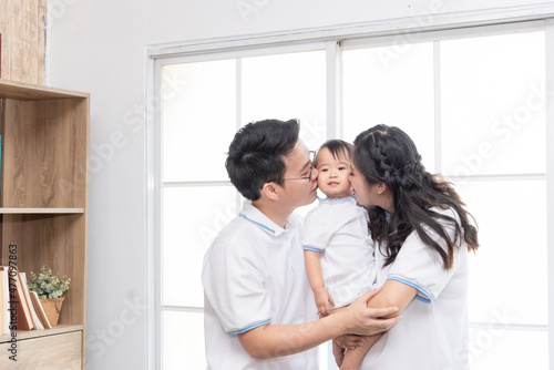 Asian happy family, father and mother kissing their baby at home.