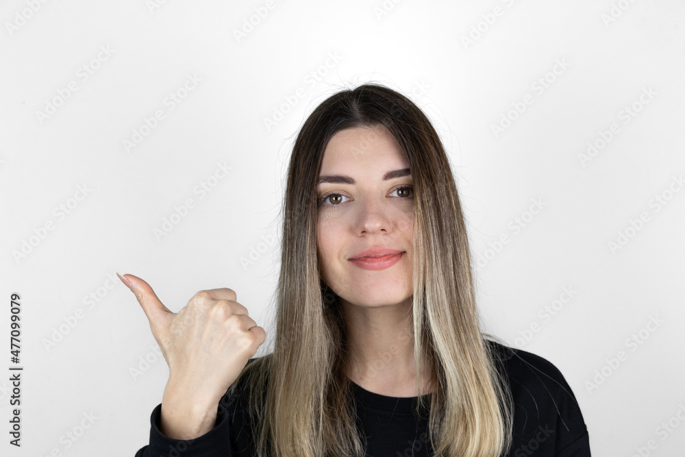 Calm lovely girl points thumb aside, shows nice place to visit or an offer, wears casual clothes, isolated on white studio background, suggets good offer or proposal. Recommend you to use copy space. Calm lovely girl points thumb aside, shows nice place to visit or an offer, wears casual clothes, isolated on white studio background, suggets good offer or proposal. Recommend you to use copy space.