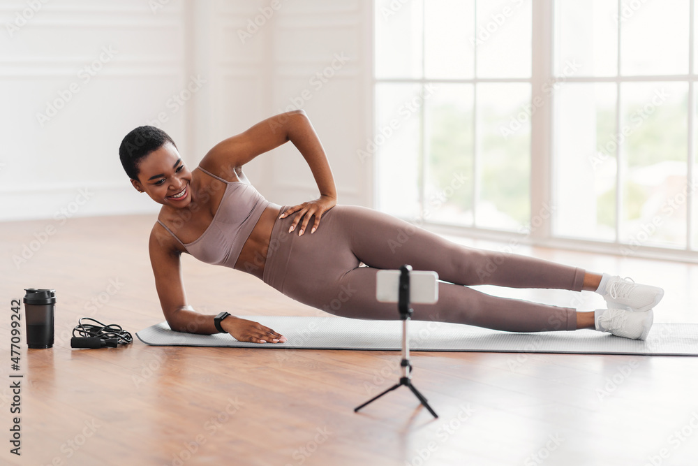 Young black woman doing side plank on mat with phone