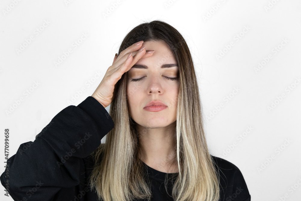Young blonde girl wearing casual clothes with hand on head for pain in head because stress. suffering migraine. White background. Young blonde girl wearing casual clothes with hand on head for pain in head because stress. suffering migraine. White background.