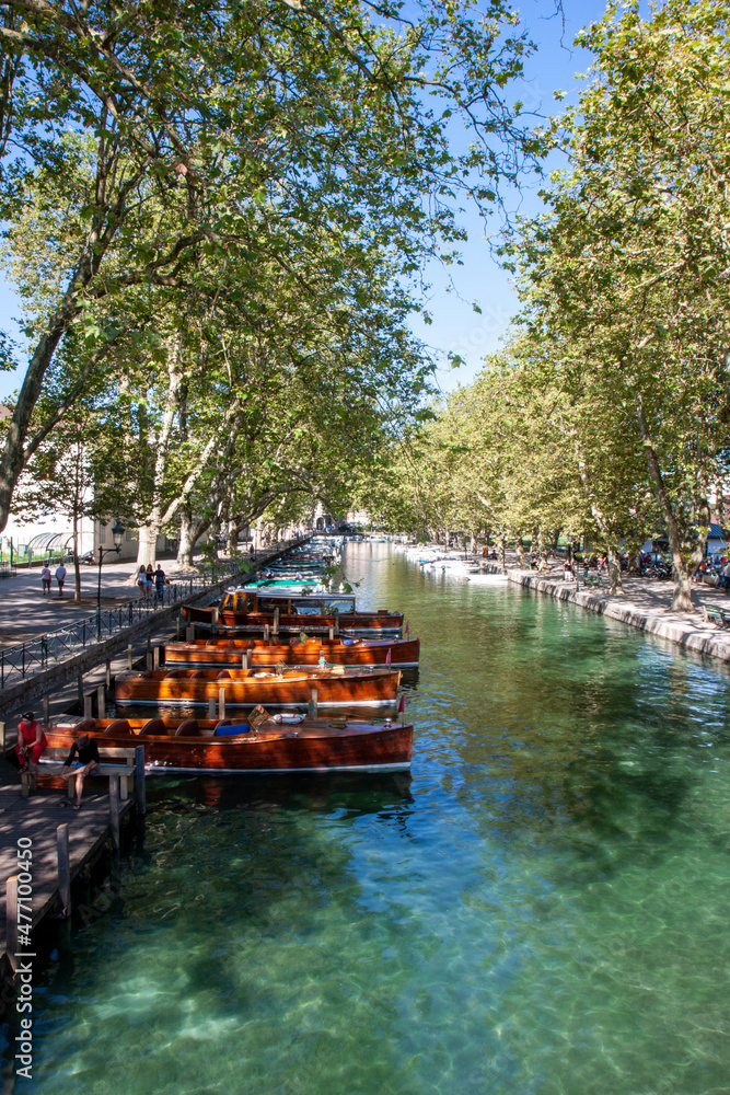 A tranquil scene with row of boats on a canal lined by trees on a summers day, in Annecy, France