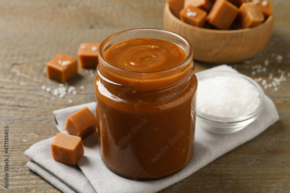 Yummy salted caramel in glass jar and candies on wooden table Yummy salted caramel in glass jar and candies on wooden table
