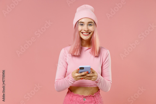 Obraz na plátně Young happy woman with bright dyed rose hair in rosy top shirt hat hold in hand use mobile cell phone isolated on plain light pastel pink background studio portrait