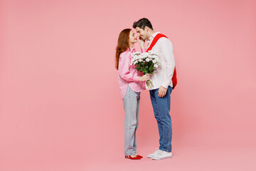 Full body side view young couple two friend woman man 20s in shirt give bouquet of flowers kiss isolated on plain pastel pink background studio portrait Valentine's Day birthday holiday party concept