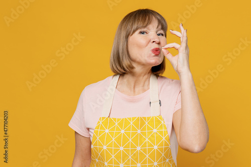 Elderly chef cooker housekeeper housewife woman 40s in orange apron show sign of good taste, belissimo gesture, kiss fingers isolated plain on yellow background. People household lifestyle concept photo