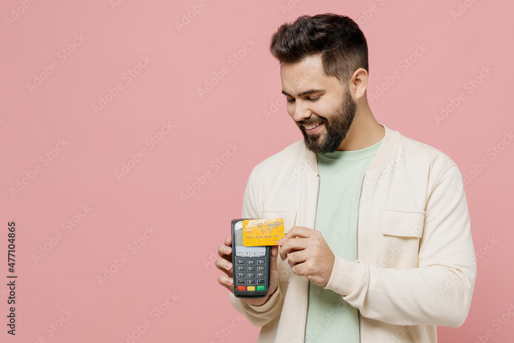Young happy fun man in trendy jacket shirt hold wireless modern bank payment terminal to process acquire credit card payments isolated on plain pastel light pink background. People lifestyle concept Young happy fun man in trendy jacket shirt hold wireless modern bank payment terminal to process acquire credit card payments isolated on plain pastel light pink background. People lifestyle concept