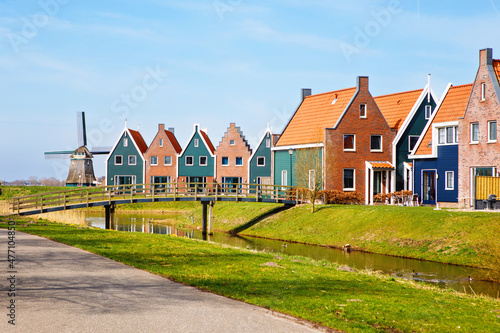 Panorama with modern brick houses along water in a family friendly suburban neighborhood in Volendam in the Netherlands. Typical Dutch houses and windmill on background. photo