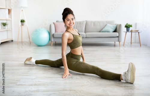 Sporty Indian woman sitting in splits, doing legs stretch, improving flexibility at home, full length