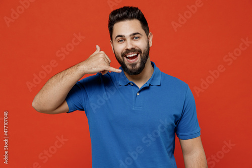 Young smiling happy caucasian man 20s wear basic blue t-shirt looking camera doing phone gesture like says call me bac isolated on plain orange background studio portrait. People lifestyle concept