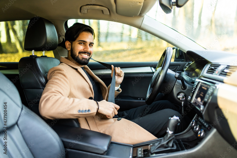 Portrait of smiling indian man fastening seat belt and sitting in his car.