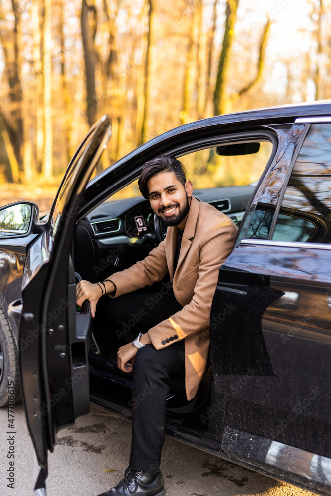 Handsome young businessman is standing near his sport car in front of modern business center Handsome young businessman is standing near his sport car in front of modern business center