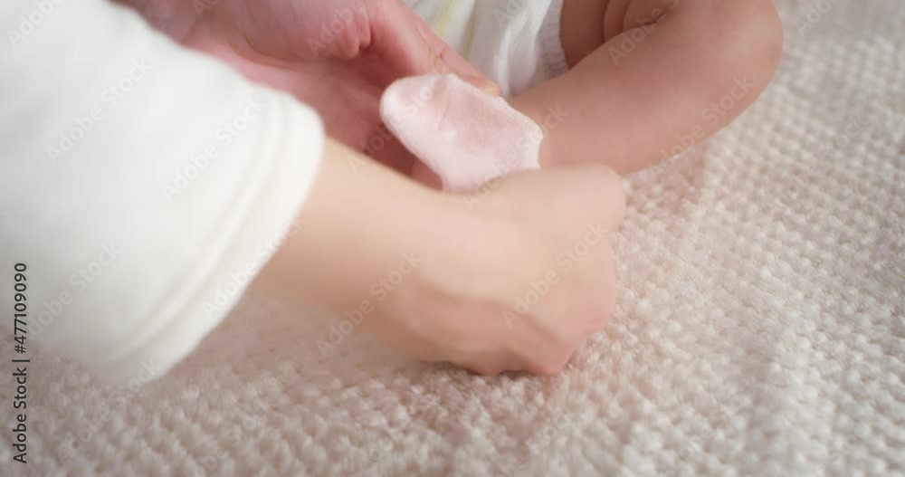 Mom lovingly puts pink socks on a newborn baby girl lying in a diaper on her back in a child crib. Authentic shots of a neonate toddler in the nursery. The concept of childhood, New life, Fatherhood Mom lovingly puts pink socks on a newborn baby girl lying in a diaper on her back in a child crib. Authentic shots of a neonate toddler in the nursery. The concept of childhood, New life, Fatherhood