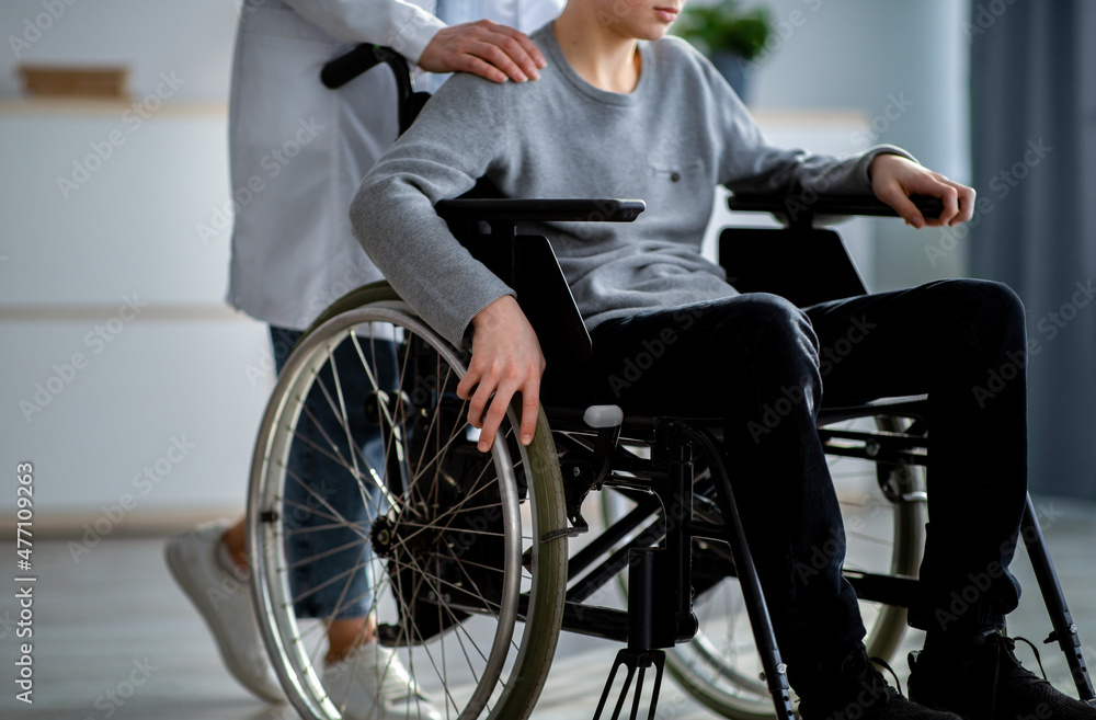 Cropped view of nurse supporting handicapped teenage boy in wheelchair at home, closeup Cropped view of nurse supporting handicapped teenage boy in wheelchair at home, closeup