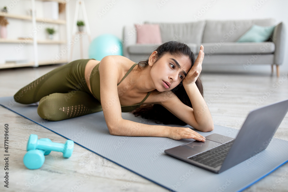 Too tired for sports. Exhausted young Indian woman lying on mat near laptop, not wishing to start online training Too tired for sports. Exhausted young Indian woman lying on mat near laptop, not wishing to start online training