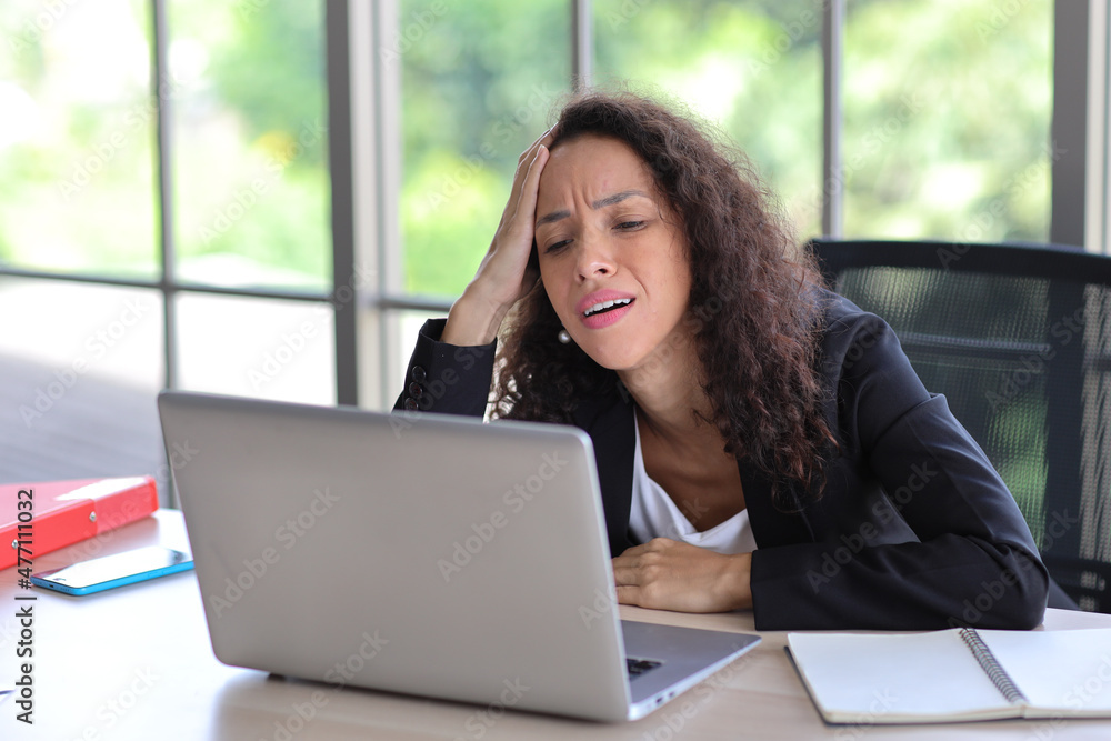 Mid adult businesswoman touching her head on table in office after bad news business failure or get fired and feeling discouraged, distraught and hopeless in modern office. Mid adult businesswoman touching her head on table in office after bad news business failure or get fired and feeling discouraged, distraught and hopeless in modern office.
