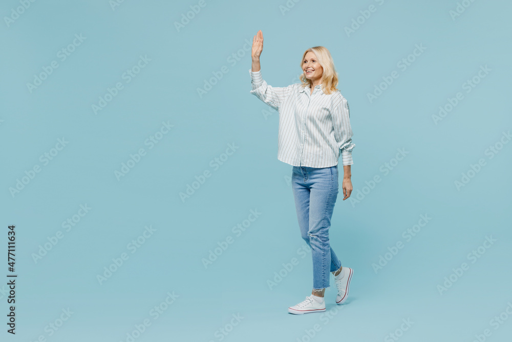 Full body elderly fun woman 50s wear casual striped shirt looking camera walk go strolling waving hand isolated on plain pastel light blue color background studio portrait. People lifestyle concept. Full body elderly fun woman 50s wear casual striped shirt looking camera walk go strolling waving hand isolated on plain pastel light blue color background studio portrait. People lifestyle concept.