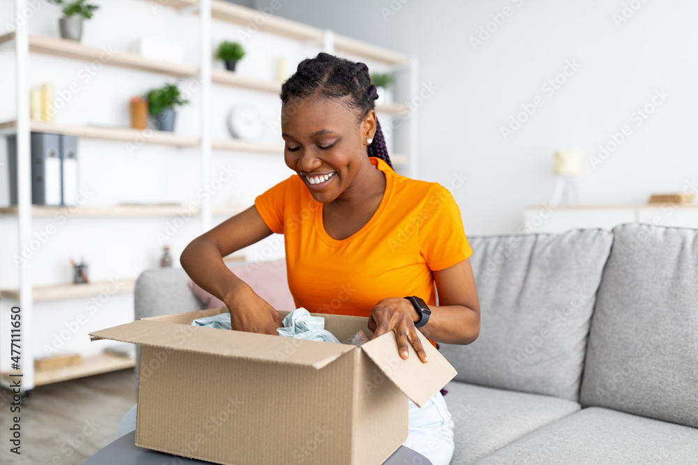 Online delivery service. Cheerful African American woman unpacking ...