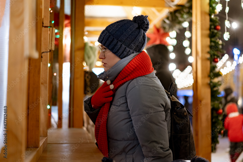 caucasian woman wearing hat and red scarf buying treats in kiosk at christmas market