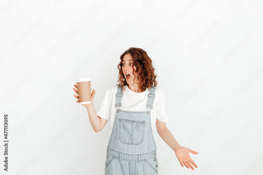 Clumsy redhead waitress, wearing denim dungarees and white t-shirt, dropping takeaway coffee cup with surprised expression over white background Clumsy redhead waitress, wearing denim dungarees and white t-shirt, dropping takeaway coffee cup with surprised expression over white background