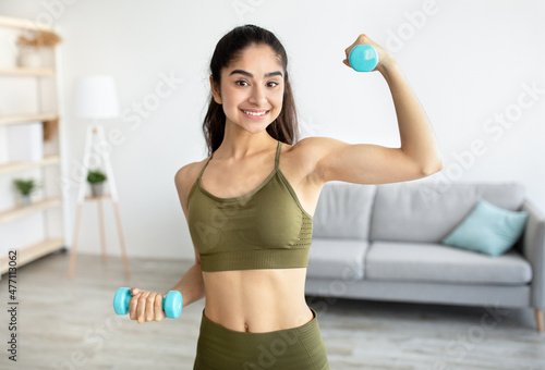 Portrait of smiling Indian woman doing domestic training, exercising with dumbbells, strengthening biceps at home