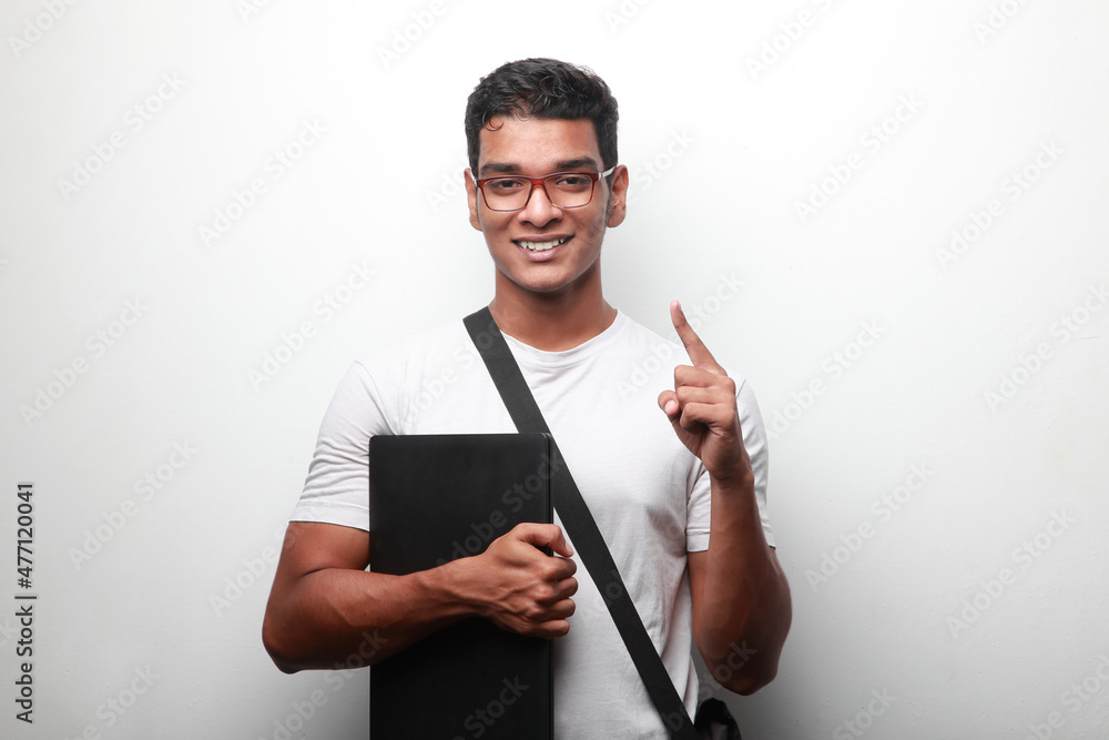 Smiling young man of Indian origin holding a laptop shows his pointed finger up Smiling young man of Indian origin holding a laptop shows his pointed finger up