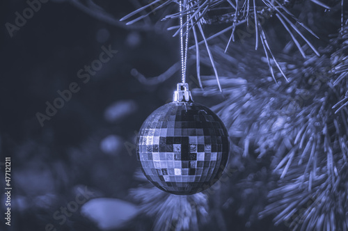 A shiny glass ball hangs on a branch of a Christmas tree. Colored in trendy color of year 2022 Very Peri. Selective focus, copy space. photo