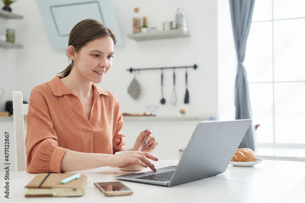 Young businesswoman typing on laptop computer at the table, she working online in the kitchen Young businesswoman typing on laptop computer at the table, she working online in the kitchen