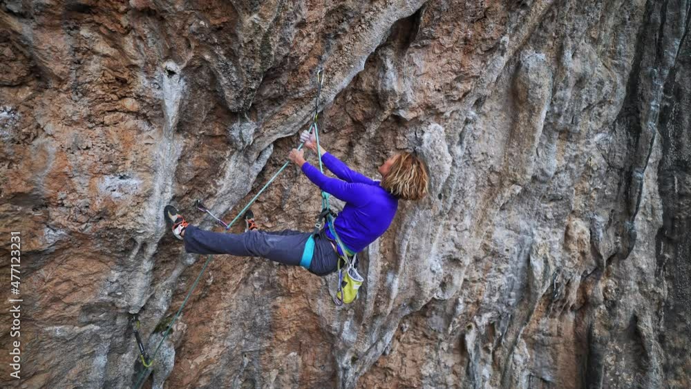 slow motion smiling tired woman rock climber hanging on rope on hard challenge route on overhanging cliff. woman resting, chalking hands and looking how to climb further slow motion smiling tired woman rock climber hanging on rope on hard challenge route on overhanging cliff. woman resting, chalking hands and looking how to climb further
