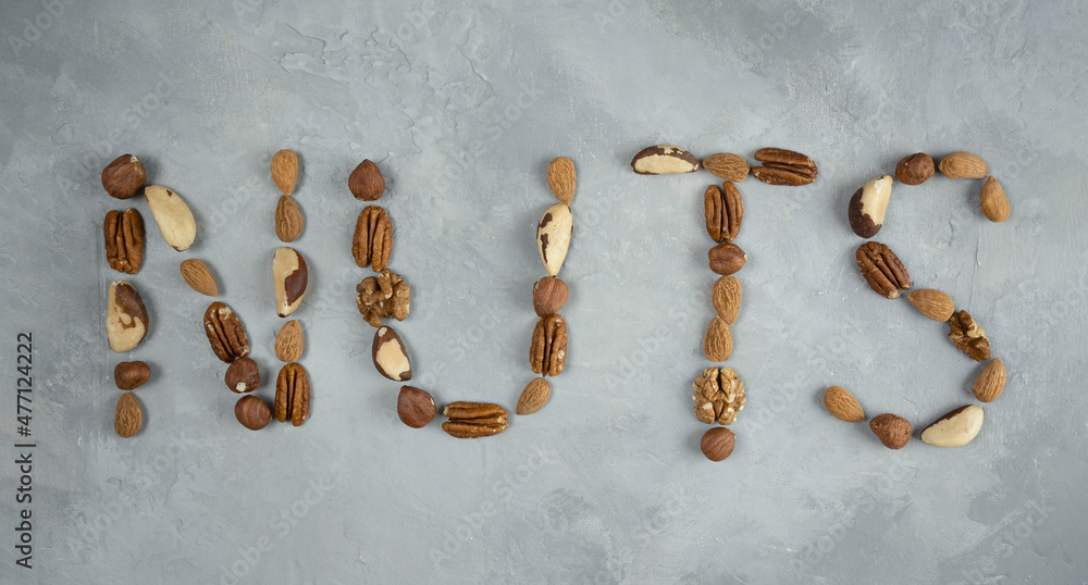 the word nuts from a mixture of nuts on a light gray background. the word nuts from a mixture of nuts on a light gray background.
