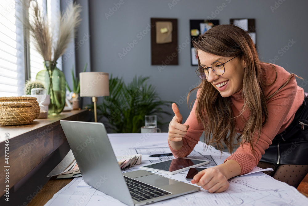Cheerful young businesswoman video chats with colleague. Beautiful young businesswoman smiles as she participates in a video conference with a colleague. She is using a laptop. Cheerful young businesswoman video chats with colleague. Beautiful young businesswoman smiles as she participates in a video conference with a colleague. She is using a laptop.