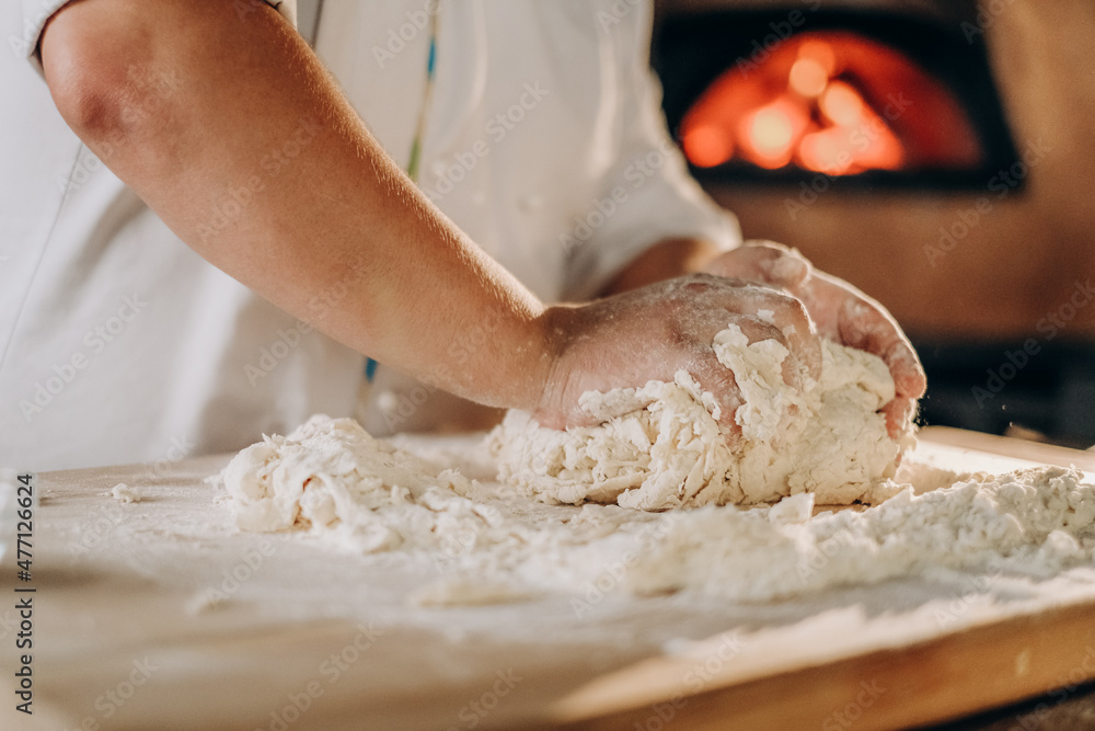 The cook prepares the pizza dough. A man kneads the dough with his hands for making pizza in the oven.