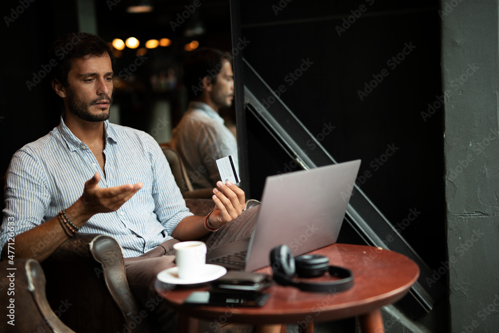 Businessman working on laptop and sitting in cafe. Young man holding credit card.