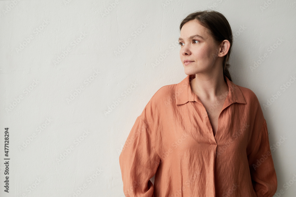 Portrait of young woman in elegant blouse posing at camera against the white wall Portrait of young woman in elegant blouse posing at camera against the white wall