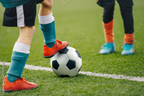 Close up image on soccer player legs with classic ball. Football background of soccer field and players in a game. Boy in sports shoes kicking ball. © matimix