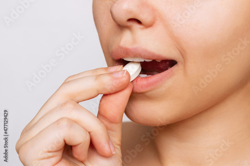 Cropped shot of a young caucasian woman taking a pill. The girl takes medications isolated on a white background. Treatment of the disease. Taking antibiotics