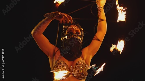 Young woman dancing performing cool and dangerous fire show and doing many tricks with fire . Dressed in black with mask closed half of face . Burning iron fire wings at night. Asian , Arabian culture photo