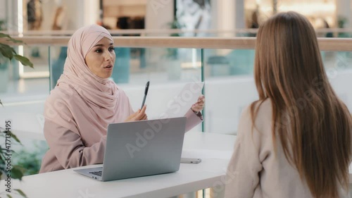 Two young girls sitting at table friendly muslim woman financial advisor explaining benefits contract manager sales agent lawyer consults with client business meeting legal consultation negotiation photo