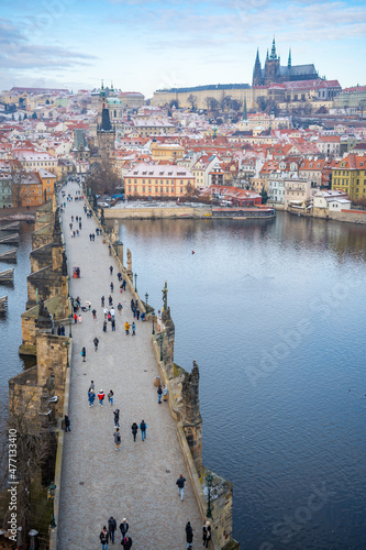 People are walking on Charles bridge, whose rooftops are covered by snow, Prague in the winter