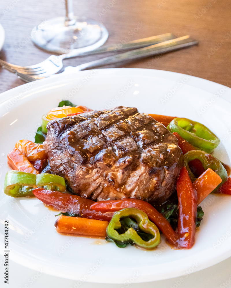 Sliced grilled meat barbecue steak with vegetables on white plate.