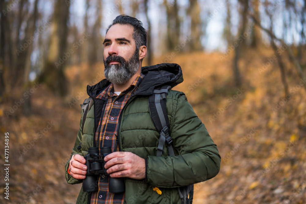 Obraz premium Image of man holding binoculars and looking at direction while hiking.