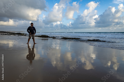 White man on the edge of the sea with his legs spread and his hands on his waist contemplating the sunrise. © Horacio Selva