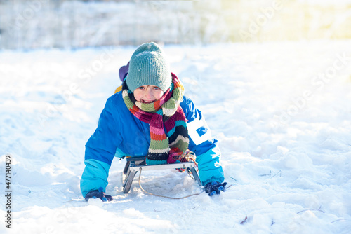 happy boy downhill on a sled in winter. a child in bright clothes sits on a sled